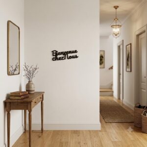 Décoration murale noire Bienvenue chez nous de 30 cm suspendue au mur d'une entrée de maison lumineuse avec un couloir en arrière-plan.