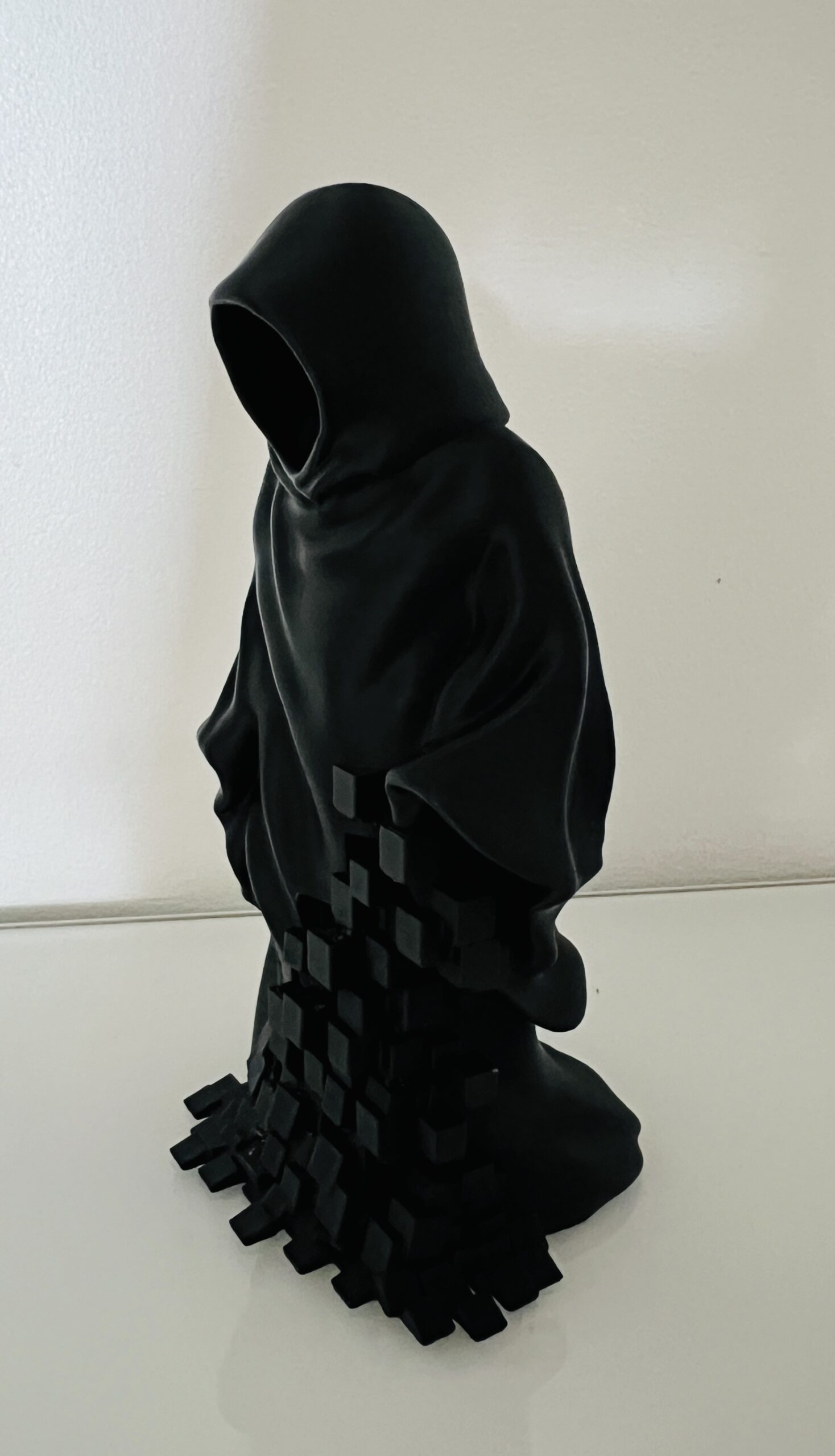 Vue de profil d'une statue de la Faucheuse noire imprimée en 3D, montrant les détails des drapés de la cape et l'effet fragmenté en petits cubes sur le bas.