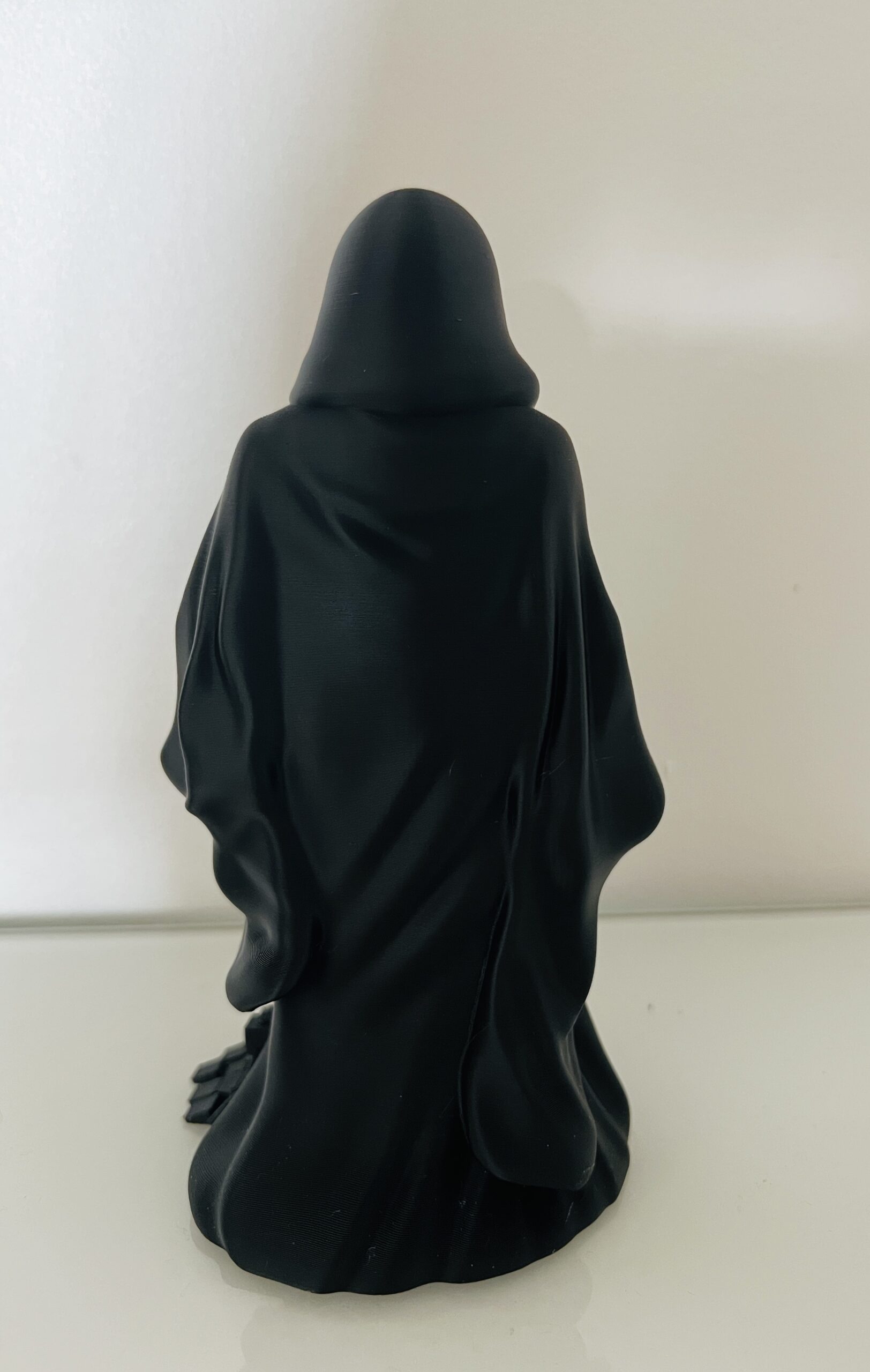 Vue arrière d'une statue décorative de Faucheuse noire imprimée en 3D, avec une longue cape détaillée et un effet de cubes en dissolution.