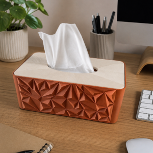 Boîte à mouchoirs design ocre et beige imprimée en 3D avec motifs géométriques, posée sur un bureau.